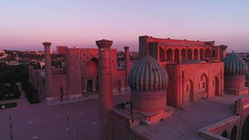 A drone flies near a complex Bibi-Khanym Mosque in Samarkand, Uzbekistan. The building is illuminated by the pink dawn light. Cloudless morning. video