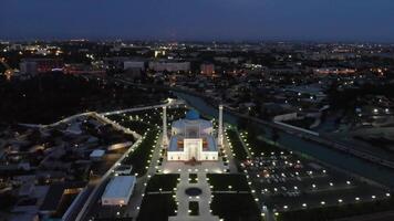 uma zangão moscas sobre uma complexo do iluminado mesquita edifícios às noite. nublado céu em a fundo. video