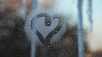 Heart shape on a foggy window against the background of icicles and winter city. video