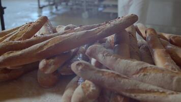 Fresh baked long baguette breads lie on the wooden table sprinkled with flour in a pile video