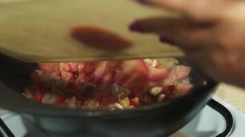 ett äldre kvinna sätter hackad tomater i en kittel med kokande olja och rör om dem med en trä- sked. video