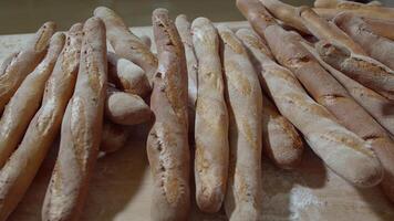 vers gebakken lang baguette brood liggen Aan de houten tafel besprenkeld met meel in een stapel video