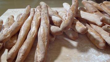 Fresh baked long baguette breads lie on the wooden table sprinkled with flour in a pile video