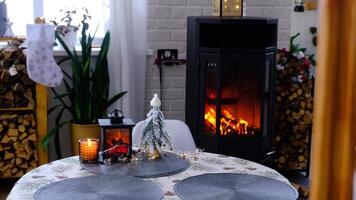 Metall black stove, burning hearth fireplace in white Festive interior of house is decorated for Christmas and New Year, Christmas tree. firewood in the woodpile, cozy and heating of home video