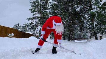 Père Noël claus nettoie neige avec pelle dans hiver en plein air après une chute de neige. nettoyage le des rues dans le village, clairière le passage pour voitures, difficile temps conditions pour Noël et Nouveau année video