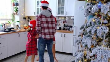 Happy traditional family of dad, mom, daughter in festive Santa hats funny and fun dancing in a white kitchen with a Christmas tree and decor. New Year, family values. video
