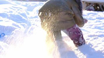 de barn flicka är rolig grävning och kasta snö utomhus, grävning snö från under själv mellan henne ben. vinter- underhållning av barndom video