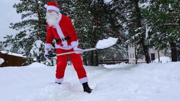 de kerstman claus reinigt sneeuw met Schep in winter buitenshuis na een sneeuwval. schoonmaak de straten in de dorp, opruimen de passage voor auto's, moeilijk weer voorwaarden voor Kerstmis en nieuw jaar video