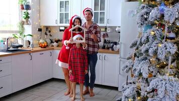 Happy family in santa hats with tiny house in cozy home with Christmas decor of festive white kitchen. Gift for New Year. Insurance, moving to new house, mortgage, rent and purchase real estate video