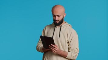 Arab guy using tablet to scroll on online websites, looking for something on the internet and using social media apps. Modern person working with touchscreen device in studio. Camera 1. video