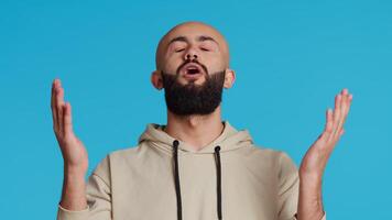 Muslim person presenting his belief in Allah by praying on camera, looking up and saying a prayer for forgiveness. Middle eastern guy worshiping God with faith, religious man in studio. Camera 2. video