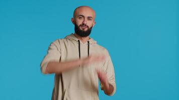 Middle eastern person doing timeout gesture on camera, asking for a break to stop working over blue background. Muslim adult presents symbol to pause or stop something. Camera 1. video