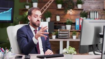 Company business worker having a video talk while siting alone in the office. In the background - monitors displaying statistics