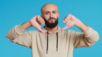 Middle eastern guy showing thumbs down sign on camera, giving dislike symbol and presenting his disappointment. Arab person feeling displeased with negative gesture in studio. Camera 2. video