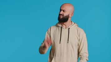 Arab male model doing no symbol on blue backdrop, showing his rejection and denial in studio. Middle eastern guy expressing refusal with a negative gesture, serious man. Camera 1. video