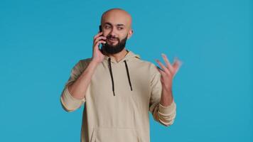 Middle eastern guy chatting with friends on phone call, answering smartphone while standing over blue background. Modern man discussing something on a remote network. Camera 1. video