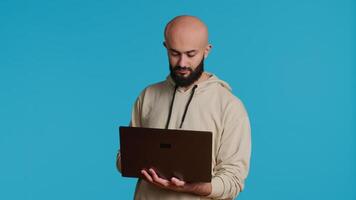 Middle eastern man works with cyber security on laptop, trying to do some software programming and report bugs. Young adult operating as a system developer in studio. Camera 1. video