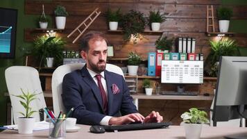 Zoom in shot of businessman working alone in office with modern design. In the background - TV and computer monitors displaying company data video