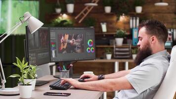 Bearded video and sound editor working on creative project in modern and cozy office with plants in the background. Freelancer and videographer