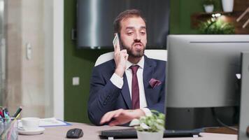 Office worker has a talk on the phone while in the background a TV displays different company data video