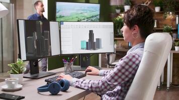 Young female architect uses a CAD or 3D software to design a new building mock-up. In the background - creative media agency office video