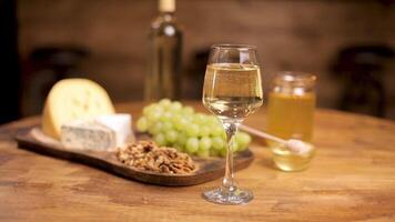 un vaso de blanco vino en un de madera mesa servido con queso y uvas. hermosa blured antecedentes de un bar mostrador en un restaurante. video