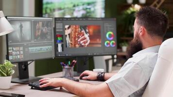 Bearded guy work as video editor or colorist in creative media agency. In the background - modern office with big TV displaying footage