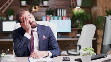 Exhausted and overworked businessman looking at clipboard with sales data. In the background - cozy and modern office video