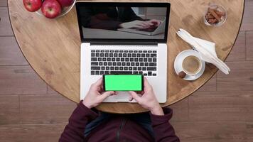 hombre en café tienda relojes un vídeo y sostiene el teléfono inteligente con verde pantalla en. insertar ninguna imagen en el teléfono inteligente pantalla. video