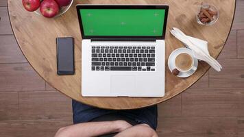 Above shot of male hands using the touchpad and the keyboard of the laptop. Computer with green screen in a vintage cafe on wooden table. video