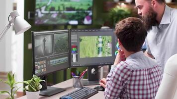 Handheld shot of professional video editor at her workstation talking with a colleague. Professional video editing and coloring software