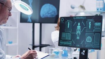 Close up shot of adult man scientists looking at advanced body scan displayed on the monitor. His team works in the background video