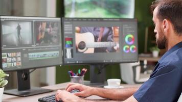 Over the shoulder shot of content creator working on his dual screen setup. Videographer and colorist video