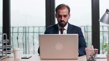 Corporate worker types on the computer on a desk in modern office with big windows. Rainy day outside video