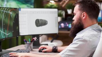 Bearded hipster architect works on 3D model of a turbine. In the background - modern creative media house video