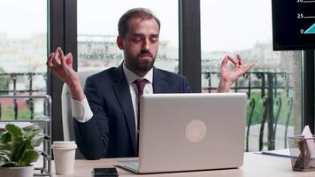 Businessman meditating in rainy day at his desk in modern office with big windows. video