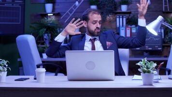 Happy and excited businessman in formal suit dances at the office desk late at night. Blue moon light through the windows. Slow motion shot video