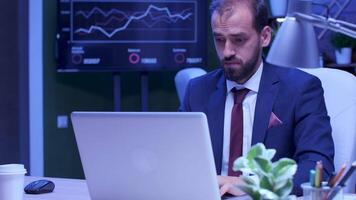 Exhausted man in formal suit works on the laptop late at night in the office video