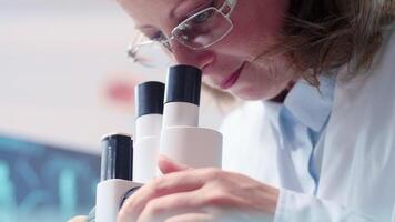 Low angle handheld shot of mature female researcher looking through a microscope. Close up shot video