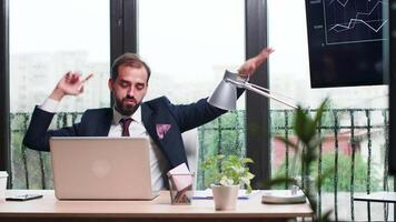 Businessman dances happily at his desk in modern office with big windows. Rainy day outdoor video