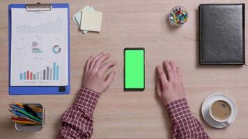 Haut vue de une homme mains toucher le bas droite coin de une vert écran sur une intelligent téléphone. au dessus coup de travail environnement concept. chrominance clé. affaires et finance. video