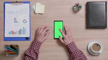 Top view of a man's hands touch the center of a green screen on a smart phone. Above shot of work environment concept. Chroma key. Business and finance. video
