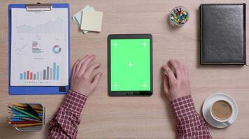 Top view of a man tap multiple times on the right bottom corner of a green screen on tablet. Office work concept. Above shot of a wooden desk. video