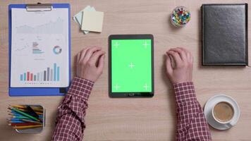 Top view of male hands scrolling on the top edge of a green screen on a black tablet. Tracking motion. Office wooden desk. Corporate concept. Chroma key. video