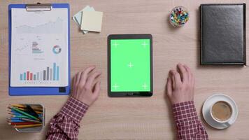 Top view of a man tap multiple times on the left bottom corner of a green screen on tablet. Office work concept. Above shot of a wooden desk. video