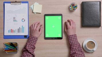 Top view of a man tap multiple times on the right top corner of a green screen on tablet. Office work concept. Above shot of a wooden desk. video