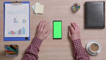 Top view of male hands scrolling on the bottom edge of a smart phone with green screen on. Above shot of work environment concept. Chroma key. Business and finance. video