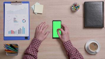 Top view of male fingers zooming in and out a green screen of a smart phone. Above shot of work environment concept. Chroma key. Business and finance. video