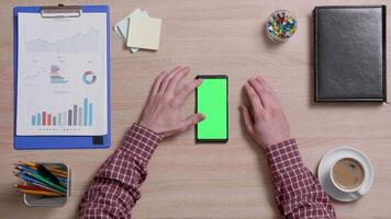 Top view of a man's hands touch the top left corner of a green screen on a smart phone. Above shot of work environment concept. Chroma key. Business and finance. video