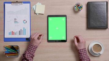 Top view of male hands scrolling on the left edge of a green screen on a black tablet. Tracking motion. Office wooden desk. Corporate concept. Chroma key. video